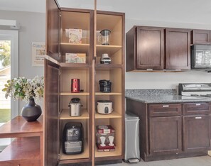 A kitchen with wooden cabinets, a microwave, a stove, and various appliances like a coffee maker and a rice cooker.