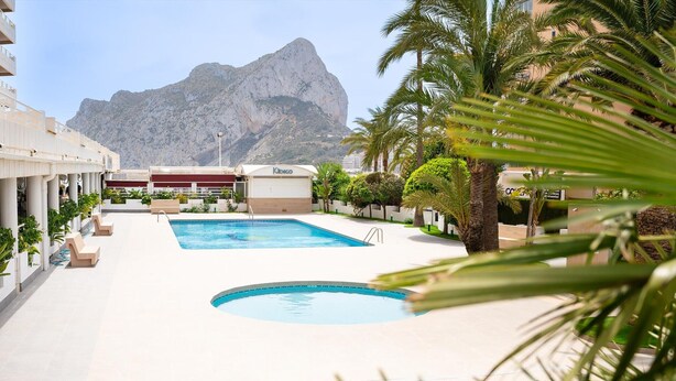Ein Swimmingpool mit Bergblick, umgeben von Palmen und einem Gebäude mit der Aufschrift 'Kibco'.