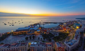 A coastal cityscape at dusk with a prominent waterfront promenade, a large circular building, and a bridge connecting the city to the sea. - Mira Home Apartment Hillside Phu Quoc (Phu Quoc)