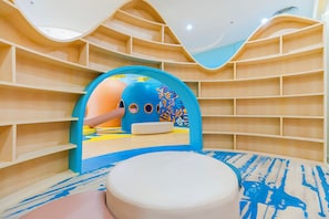 Ein Kinderspielbereich mit Tunnel, Regalen und einer runden Sitzecke.