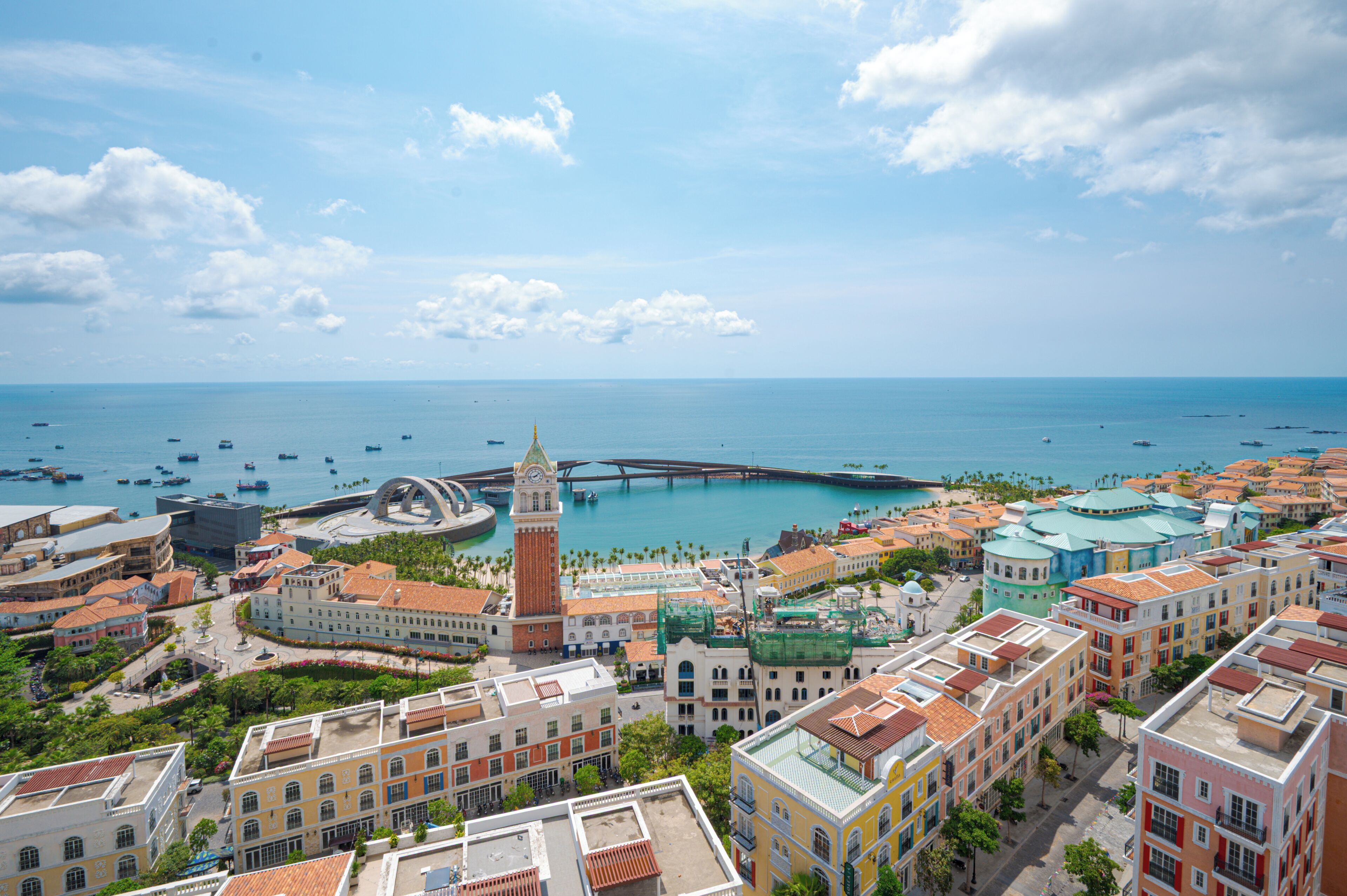 A coastal cityscape with a prominent clock tower, a bridge, and a marina with boats.