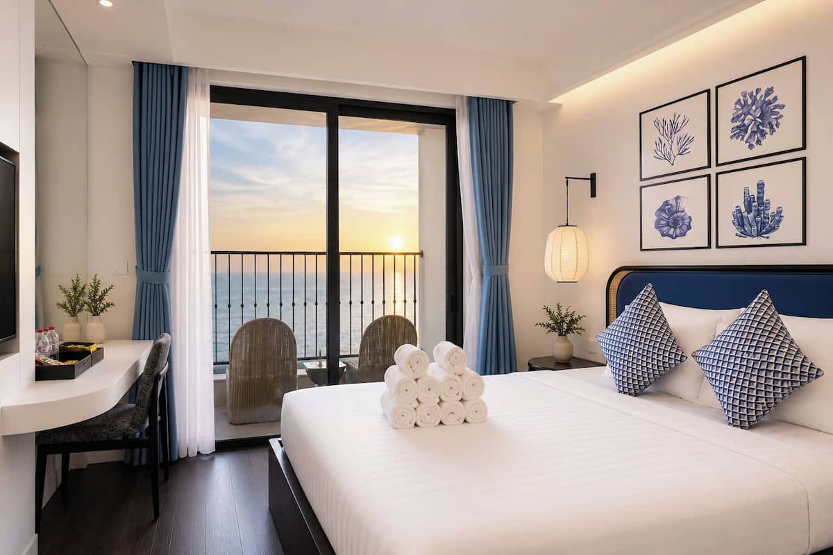 Habitación de hotel con cama, escritorio, silla y vista al mar, además de una obra de arte en la pared.