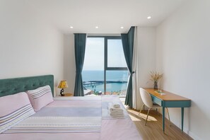 Un dormitorio con cama, escritorio, silla y vista al mar.