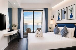 A hotel room with a bed, a desk, a chair, a TV, and a balcony with a view. - Mira Home Apartment Hillside Phu Quoc (Phu Quoc)