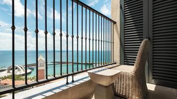 A balcony with a view of the sea, a chair, and a table.