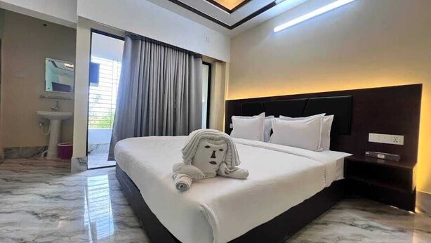 Une chambre d’hôtel avec un grand lit, une tête de lit, une table de chevet, un miroir et une salle de bain équipée d’un lavabo, le tout offrant une vue sur l’extérieur.