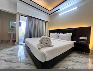 A hotel room with a large bed, a headboard, a bedside table, a mirror, a bathroom with a sink, and a view of the outdoors. - The Vacation Inn Hotel & Resort (Bandarban)