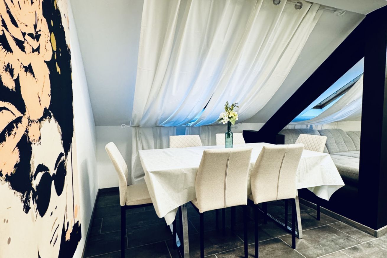 A dining area with a table set for four, white curtains, and a vase with flowers.