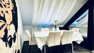 A dining area with a table set for four, white curtains, and a vase with flowers.