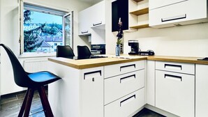 Een moderne keuken met witte kasten, een houten aanrecht, een koffieapparaat en uitzicht op een woongebied.