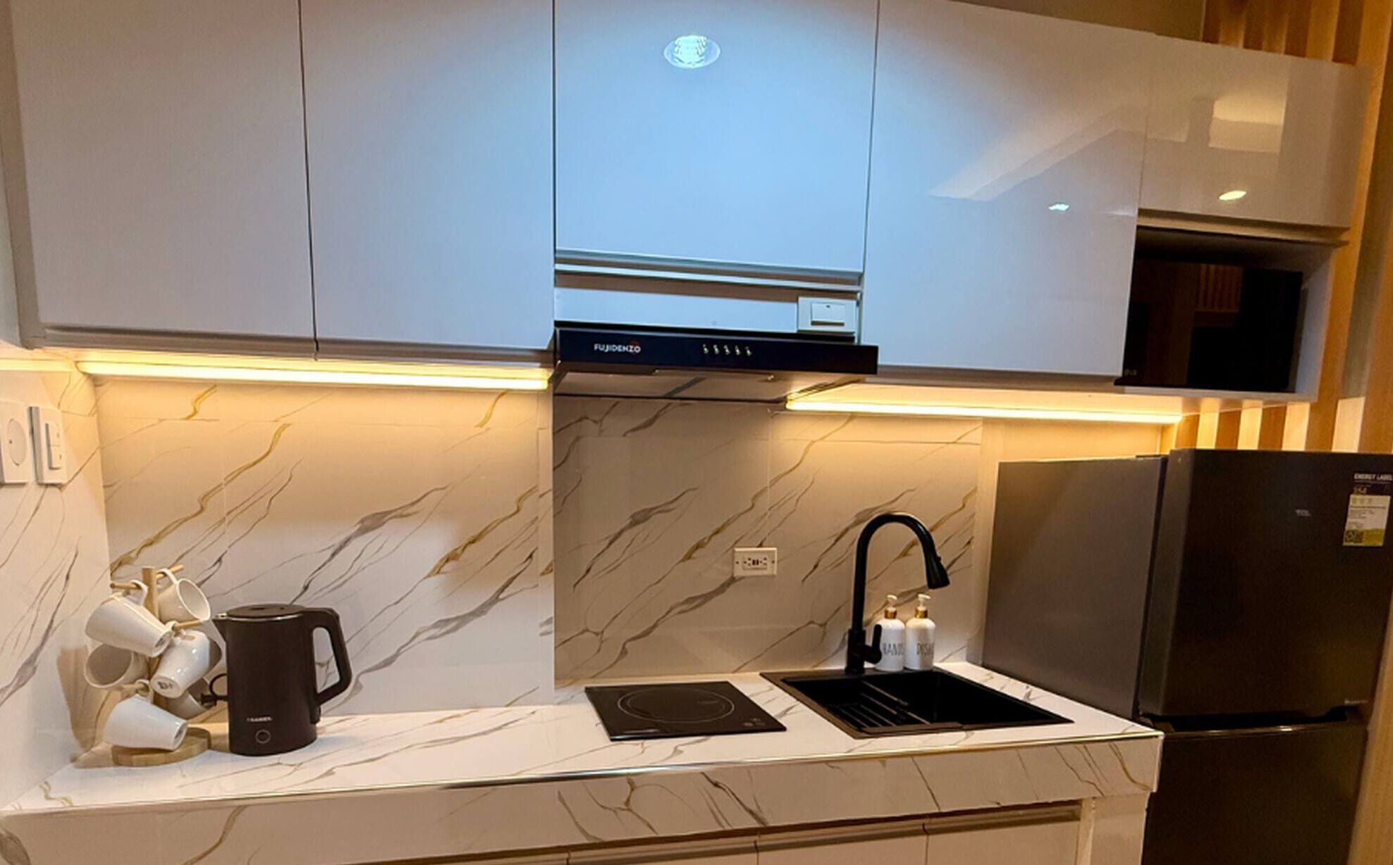 Une cuisine moderne avec des meubles blancs, une cuisinière encastrée, un évier et un réfrigérateur.