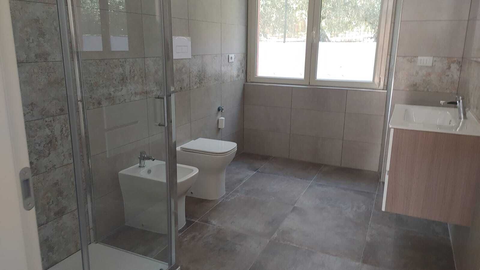 A bathroom with a glass shower enclosure, a bidet, a toilet, and a sink.