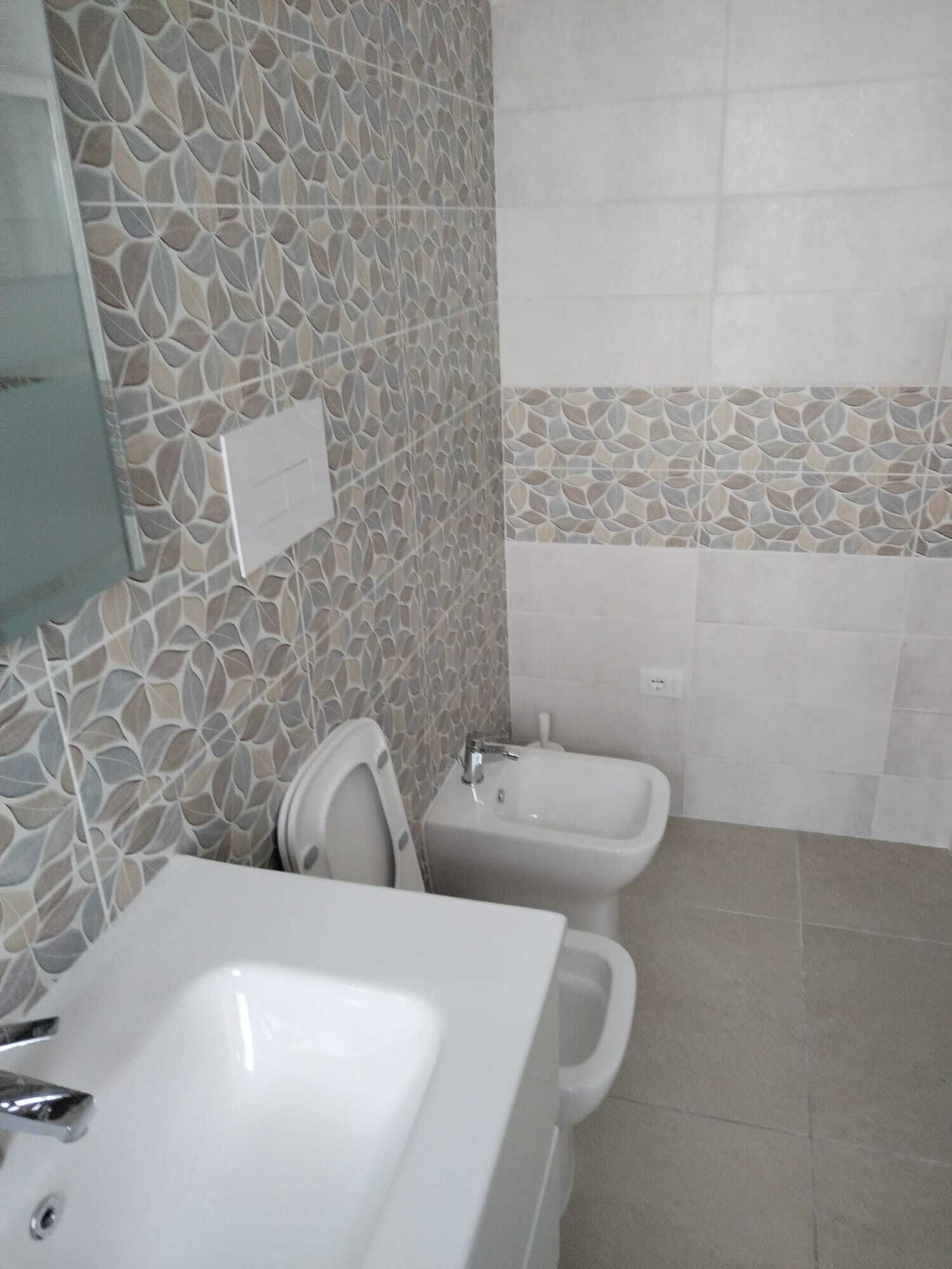 Une salle de bain avec un lavabo blanc, des toilettes et un bidet. Les murs sont recouverts de mosaïques.