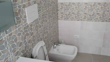 Une salle de bain avec un lavabo blanc, des toilettes et un bidet. Les murs sont recouverts de mosaïques.
