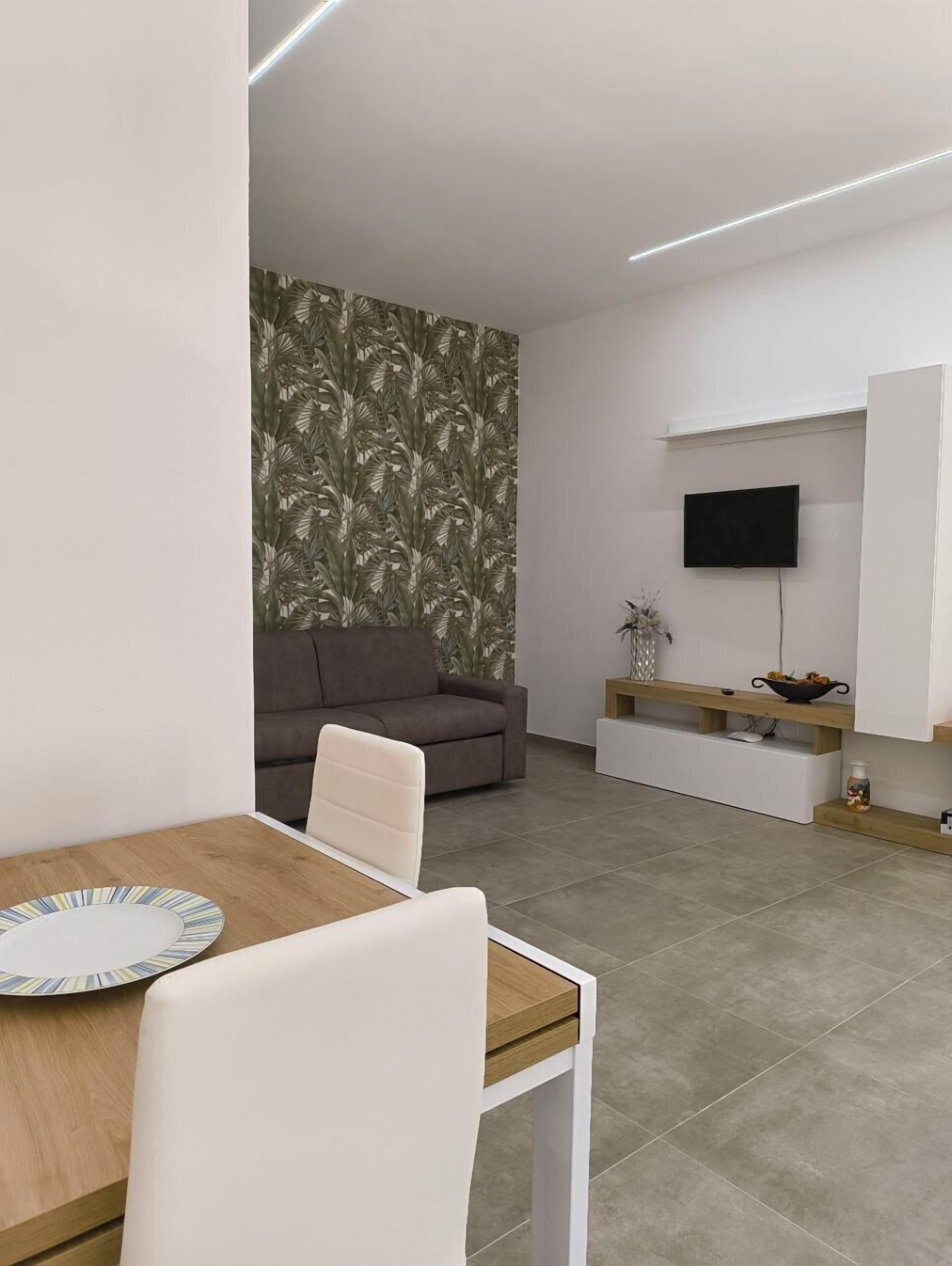 Una sala de estar moderna con un sofá, un televisor montado en la pared y una zona de comedor con una mesa y sillas.
