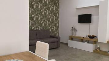 Una sala de estar moderna con un sofá, un televisor montado en la pared y una zona de comedor con una mesa y sillas.