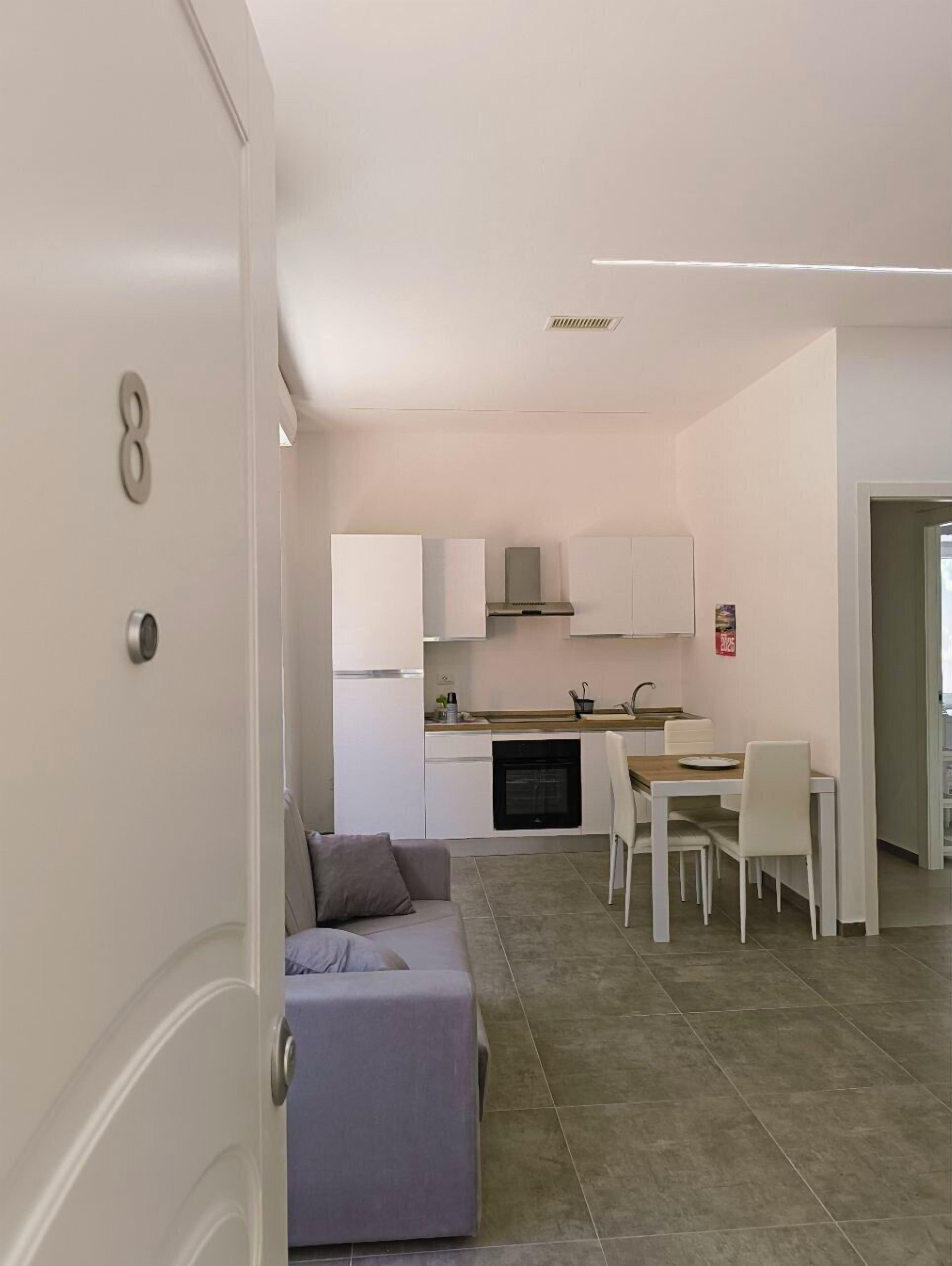 A modern kitchen with white cabinets, a built-in oven, and a dining area with a table and chairs.
