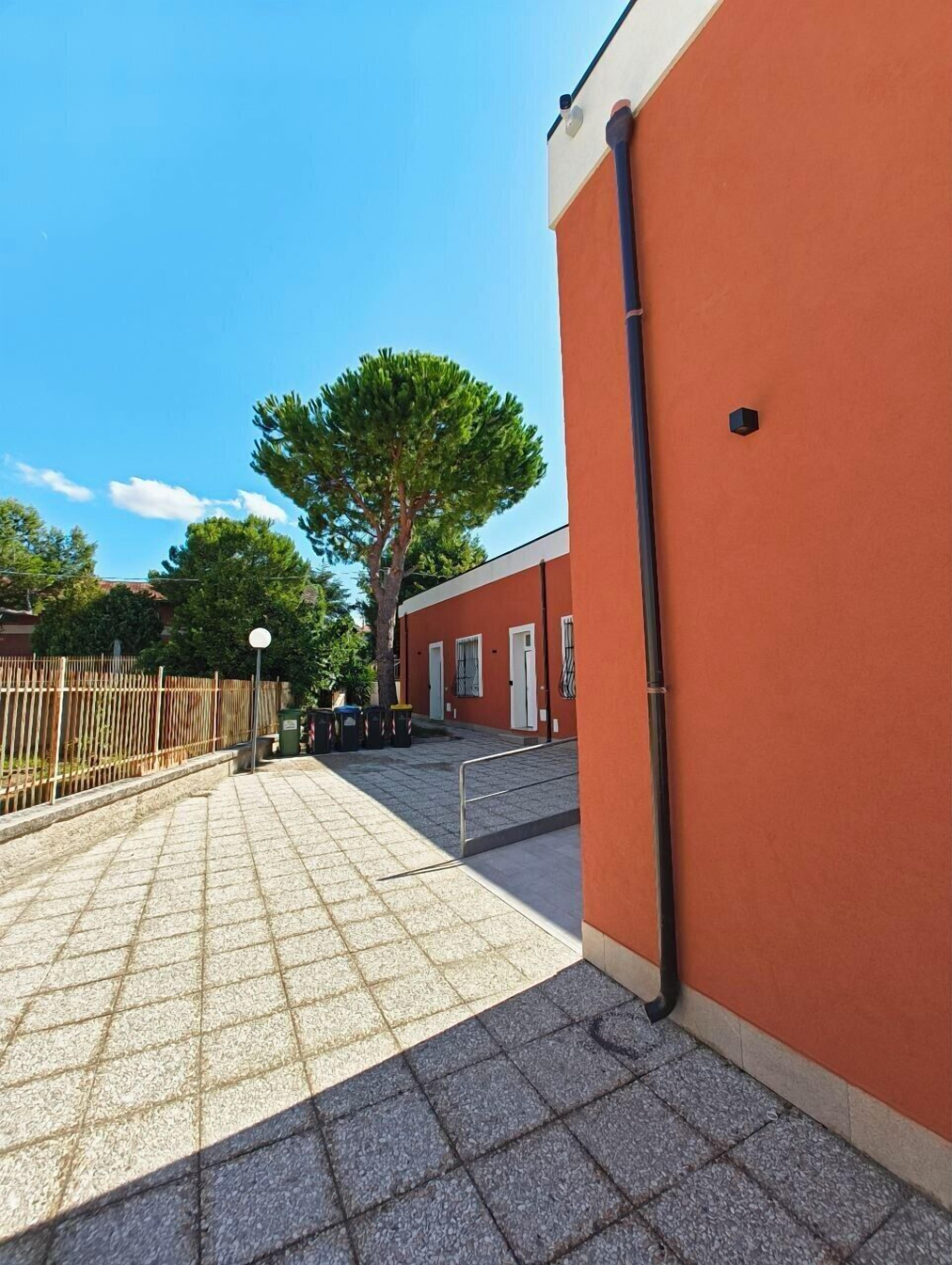 Ein gepflasterter Innenhof mit Fliesenboden, einem Metallzaun und einem großen Baum.