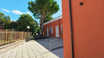 Ein gepflasterter Innenhof mit Fliesenboden, einem Metallzaun und einem großen Baum.