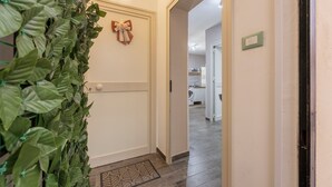 Un pasillo con un muro cubierto de plantas verdes, una puerta decorada con un lazo y un felpudo estampado.