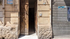 Una puerta de madera abierta que da a un edificio, una puerta metálica con persiana cerrada, y un letrero con un número de teléfono.