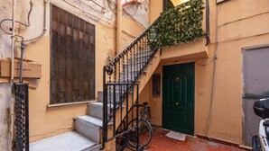 Una escalera estrecha con barandilla de metal, una puerta verde y una bicicleta apoyada contra la pared.