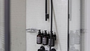 Une salle de bain avec un mur carrelé, une pomme de douche et trois bouteilles de shampoing.