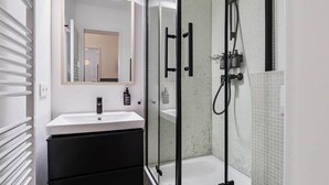 Une salle de bain moderne avec une douche à parois de verre, un lavabo blanc et un meuble noir.