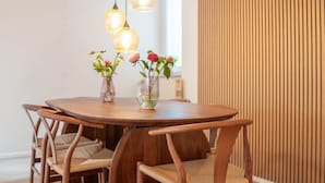 Une table de salle à manger ronde en bois, accompagnée de quatre chaises, de deux lampes suspendues et de deux vases de fleurs.