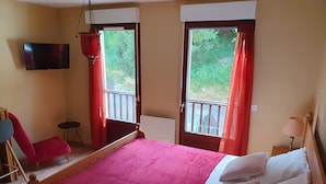 A bedroom with a bed, a chair, a TV, and a balcony with curtains. - Studio in residence near Lourdes / Vallée des Gaves (Aspin-en-Lavedan)