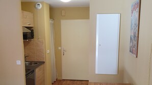 A compact kitchen with a microwave, a sink, and a dishwasher. There is a dining area with a wooden table and two blue chairs. - Studio in residence near Lourdes / Vallée des Gaves (Aspin-en-Lavedan)