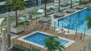 Un espace piscine aménagé sur le toit, avec des palmiers, des chaises longues et une vue sur le paysage urbain.
