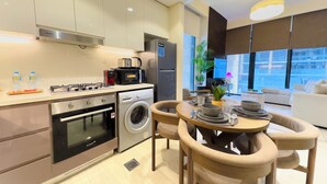 Une cuisine moderne équipée d’une cuisinière à gaz, d’un four, d’un lave-linge et d’une machine à café. On y trouve un coin repas avec une table ronde et des chaises, ainsi qu’un canapé dans le salon.