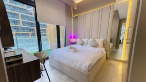 Une chambre d’hôtel moderne, dotée d’un grand lit, d’un bureau et offrant une vue sur la ville grâce à de grandes fenêtres.