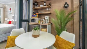 Ein modernes Hotelzimmer mit einem Bett, einem runden Esstisch mit zwei Stühlen, einer Kaffeemaschine und einem kleinen Topfpflanzen.