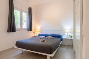 Une chambre à coucher avec un lit, deux tables de chevet, une fenêtre avec des rideaux et une petite table de nuit avec une lampe.