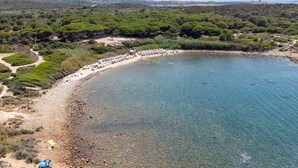 A coastal area with a beach, clear water, and dense greenery.