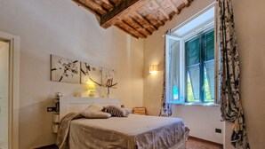 A bedroom with a bed, a nightstand, a lamp, a window with curtains, and artwork on the wall.