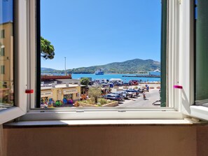 A view through a window of a coastal area with parked cars, a boat dock, and a building labeled 'EDICOLA DEL PONTES.'