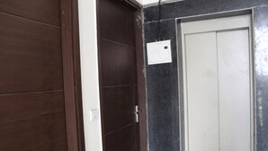A hallway with a wooden door and a white door with a light switch on the wall. - Star Light Inn (New Delhi)