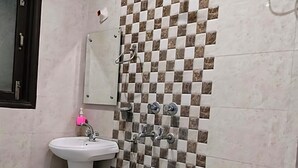 A bathroom with a checkered tile wall, a white sink, and a toilet. - Star Light Inn (New Delhi)
