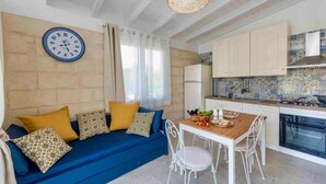 A cozy living area with a blue sofa, a dining table, and a kitchen with light-colored cabinets and a tiled backsplash.
