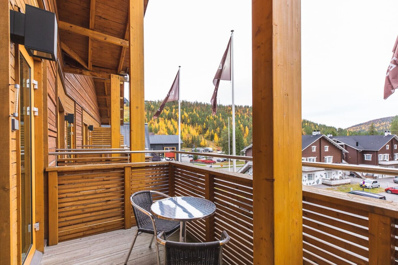A wooden deck with a table and chairs, overlooking a residential area with houses and a forested hill.