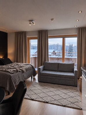 Une chambre à coucher moderne, avec un lit, un canapé et une vue sur un paysage enneigé, visible à travers de grandes fenêtres.