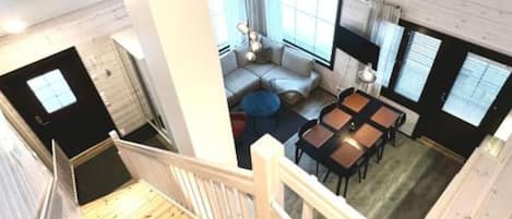 A modern interior with a wooden staircase, a seating area with a sofa and tables, and large windows providing natural light.