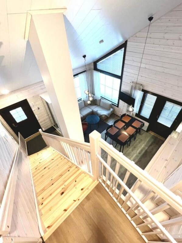 A modern interior with a wooden staircase, a seating area with a sofa and tables, and large windows providing natural light.