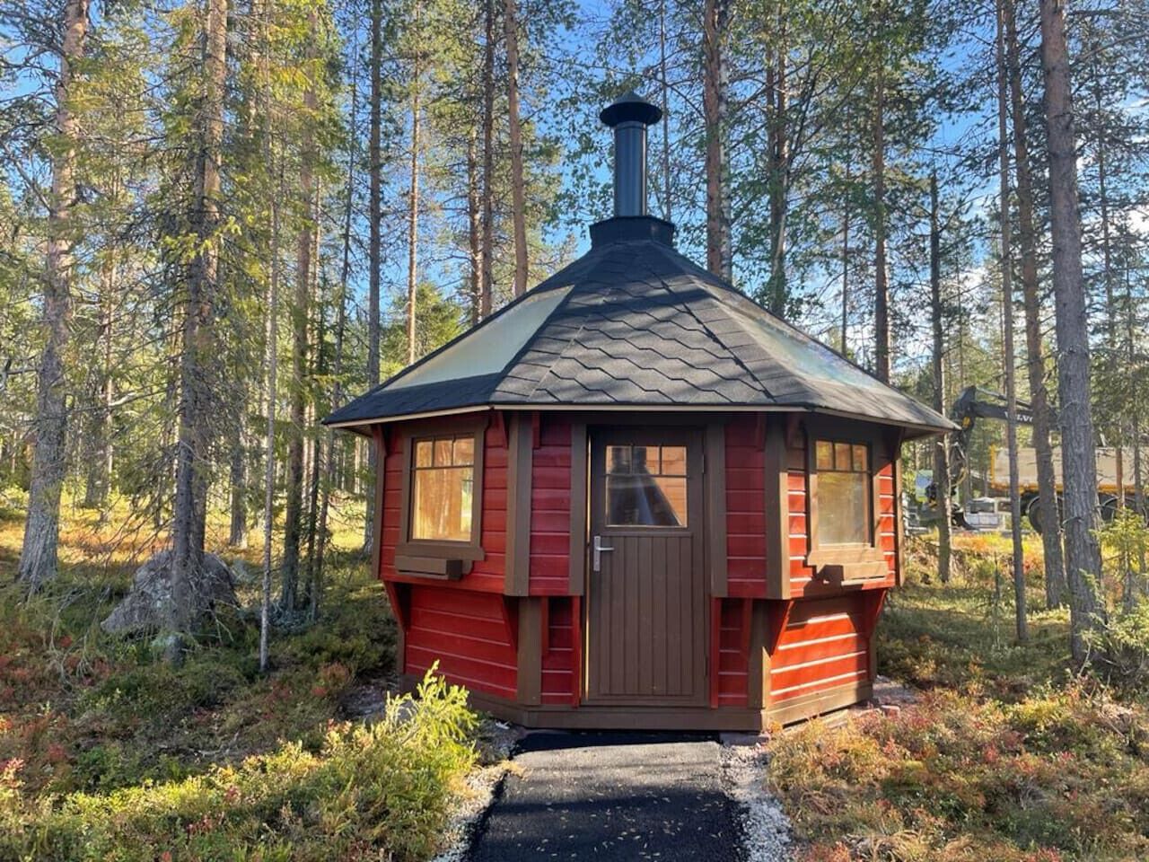 Een klein, rood vakantiehuisje met schoorsteen, omgeven door een bos.
