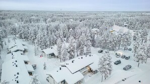 A snow-covered residential area with multiple houses, a parking lot, and a large open field in the background. - Cozy apartment in the center of Levi (Levi)