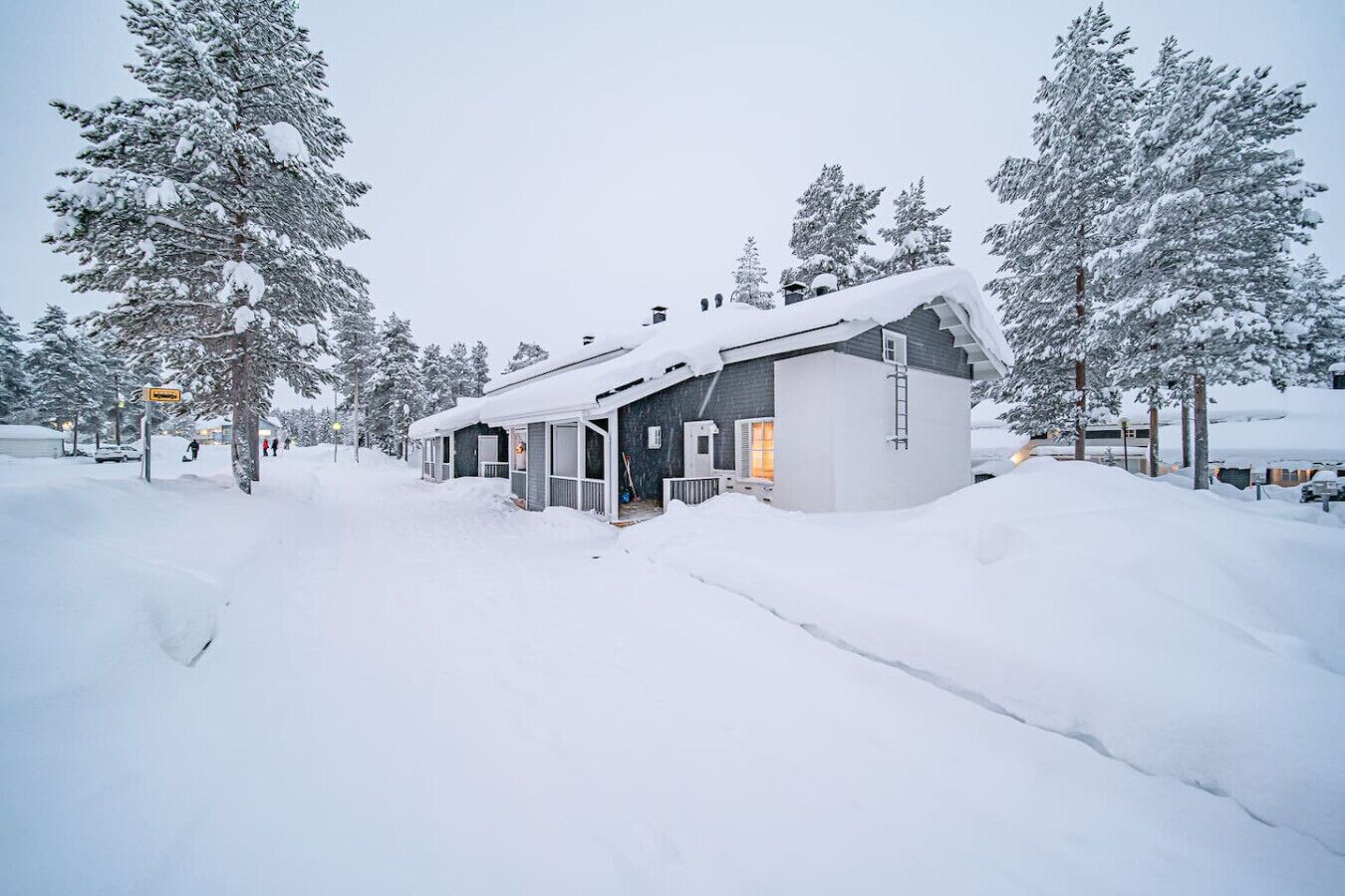 A snow-covered lodge with a large porch and a chimney, surrounded by snow-laden trees.