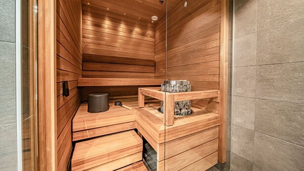 Een sauna met houten wanden en banken, een klein tafeltje met een bak, en een verwarmingselement.